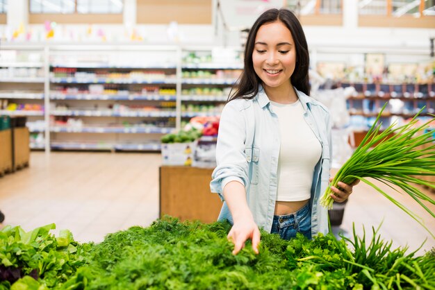 Happy Asian woman picking greenery in grocery store