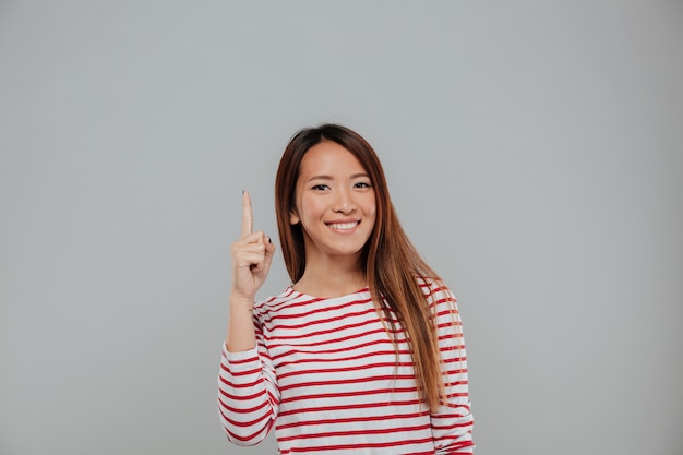 Счастливая азиатская женщина указывая палец вверх на космос экземпляра