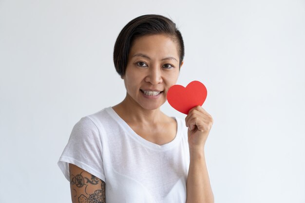 Счастливая азиатская женщина представляя с бумажным сердцем