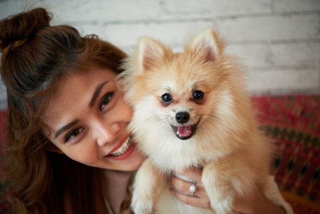 幸せなアジア女性が小さなペットの犬を自宅でポーズ