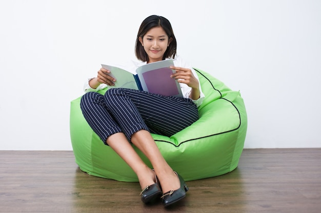 Happy asian woman reading magazine on beanbag