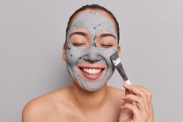 幸せなアジアの女性は化粧マスクを受け取り、ブラシの笑顔を広く使用しています