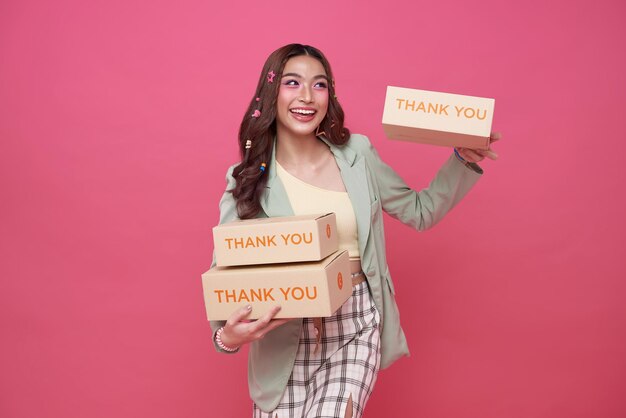 Счастливая азиатка улыбается и держит коробку с посылкой на розовом фоне