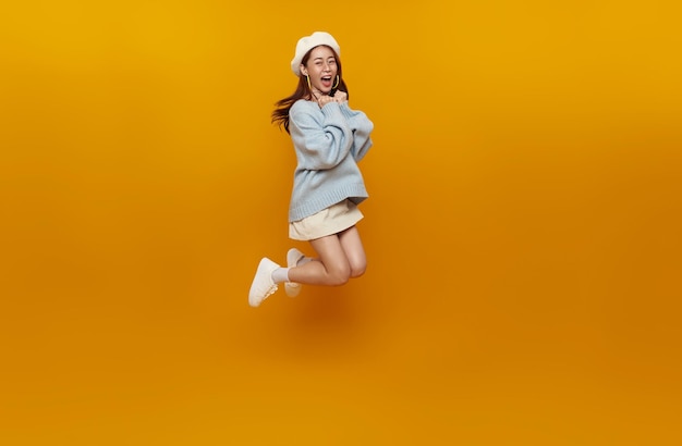 Happy Asian woman smiling and jumping while celebrating success isolated over yellow background