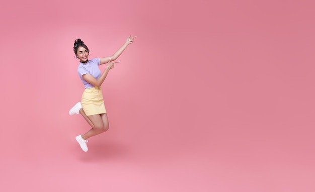 Happy Asian woman smiling and jumping while hands pointing isolated over pink background copy space