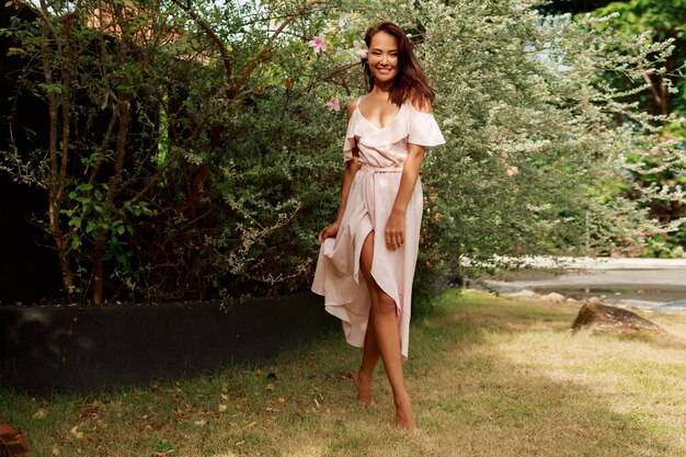 Happy Asian woman with candid smile in pink dress posing in summer garden