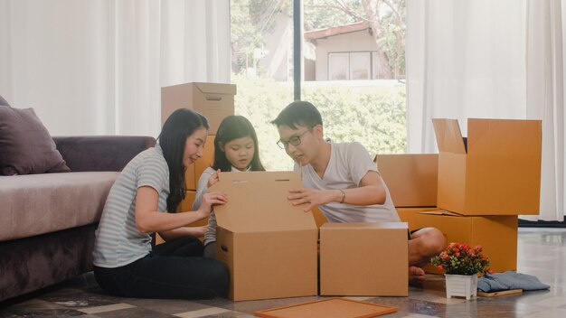 Happy Asian young family relocation removals settle in new home. Chinese parents and kids open cardboard box or parcel unpacking in living room on moving day. Real estate dwelling, loan and mortgage.