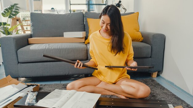 Happy asian young woman unpacking box and reading the instructions to assemble new furniture