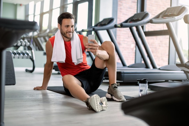 Happy athletic man text messaging on cell phone in health club