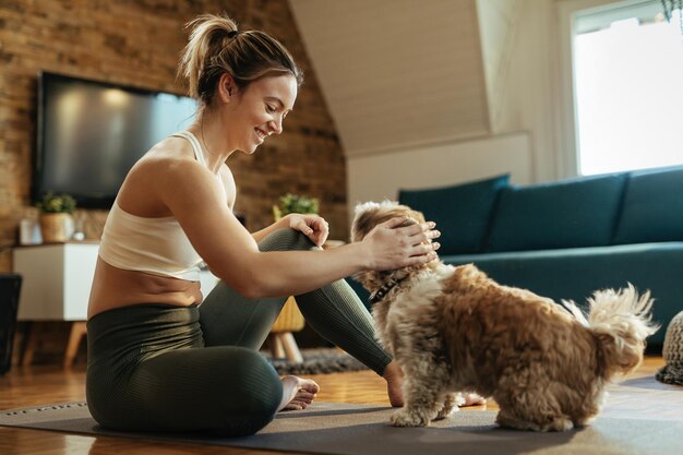 Happy athletic woman sitting on the floor and having fun with her dog at home