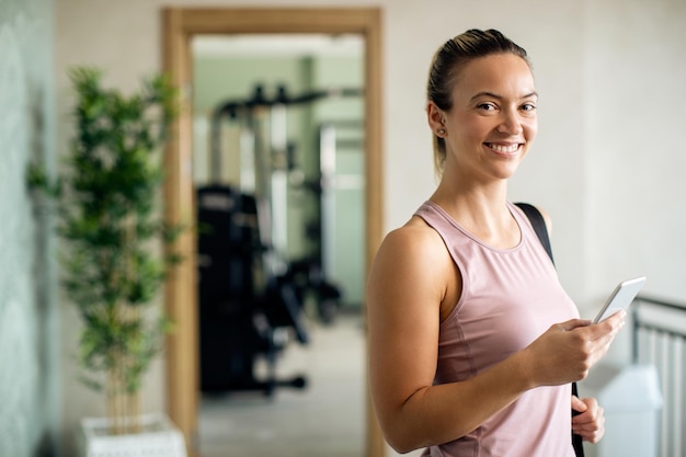 Happy athletic woman using smart phone in a hallway at health club