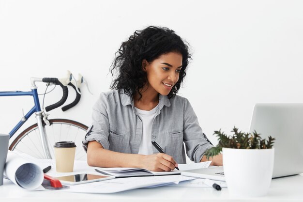 Happy attractive experienced African American female designer writing down some measured data