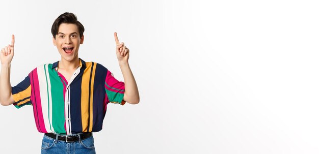 Happy attractive gay man pointing fingers up smiling excited showing top offer standing over white background