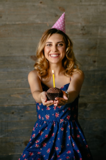 Free photo happy attractive girl holds a chocolate cupcake with candle, celebrating her birthday