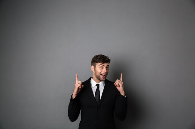 Счастливый привлекательный парень в черном костюме, указывая двумя пальцами вверх