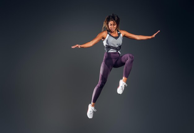 Счастливая привлекательная женщина в спортивной одежде прыгает в студии на сером фоне.
