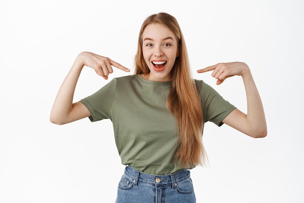 Happy attractive woman pointing at herself and smiling bragging personal achievements being chosen picked from candidates standing selfpromoting against white background