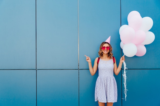 Happy attractive woman in sunglasses and party hat, holds air balloons