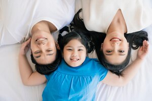 Happy attractive young asian family portrait healthy harmony in life family day concept asian family man woman and little girl having good time togethertop view bedroom mattress