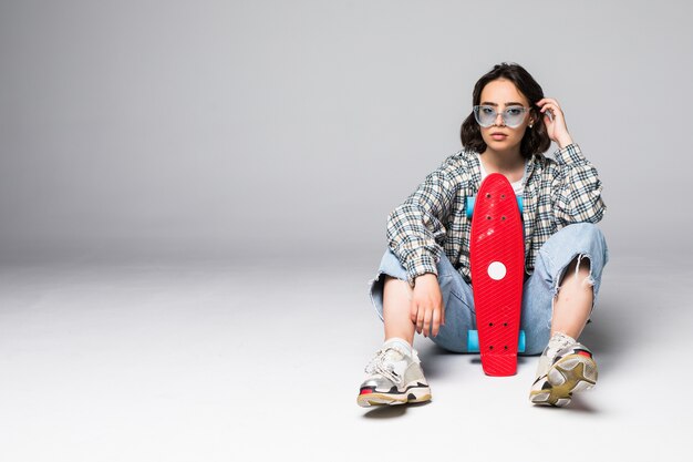 Happy attractive young woman in sunglasses sitting on skateboard