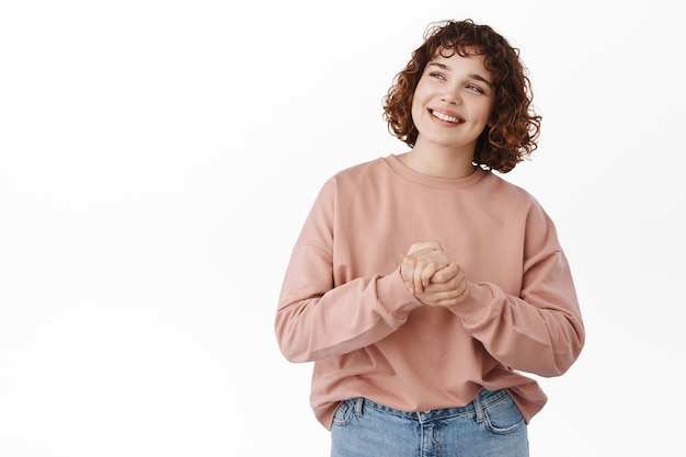 Felice ragazza autentica sorridente, guardando il logo promozionale nell'angolo in alto a sinistra, leggendo la pubblicità con una faccia allegra e soddisfatta, sognando ad occhi aperti, in piedi su sfondo bianco.