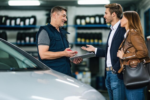 ワークショップで若いカップルと通信する幸せな自動車修理工