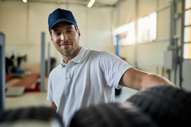 Happy auto repairman taking car tire form a rack in a workshop