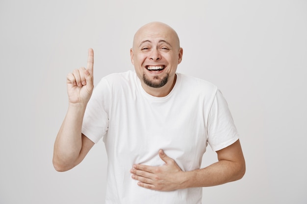 Happy bald middle-aged man laughing over copyspace, pointing up as chuckle