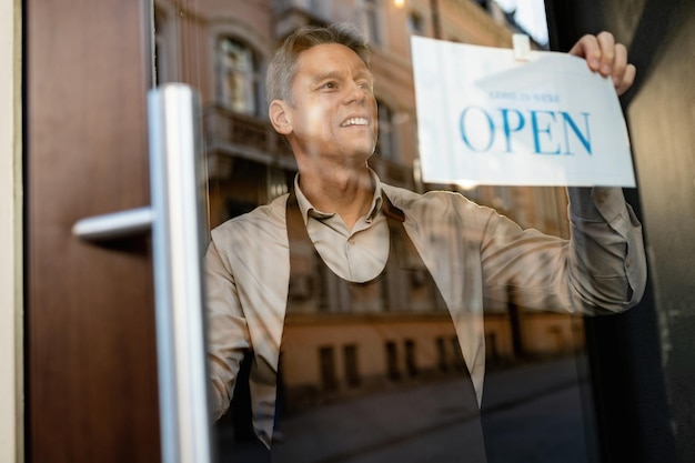 Foto gratuita felice barista appeso segno aperto sulla porta d'ingresso di un bar