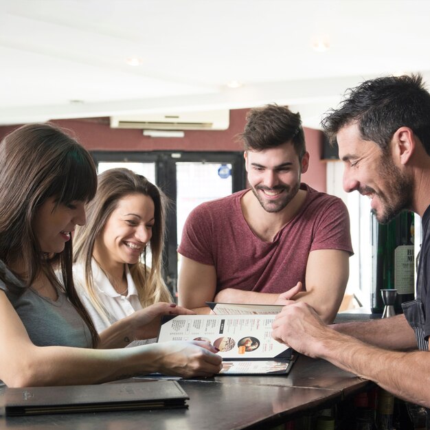 Happy barman and customers looking at menu in the bar