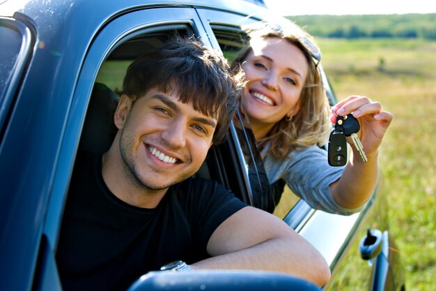 新しい車に座っている鍵を見せて幸せな生意気なカップル