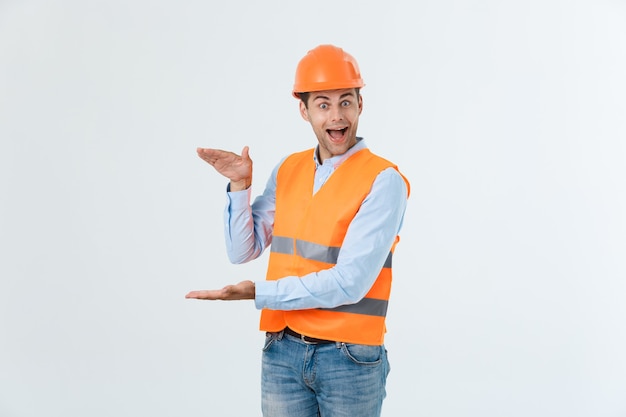 Happy beard engineer holding hand on side and explaining something, guy wearing caro shirt and jeans with yellow vest and orange helmet, isolated on white background.