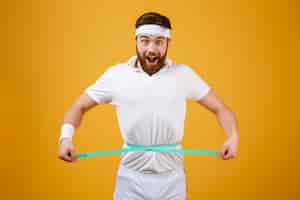 Free photo happy bearded fitness man measuring his waist with tape