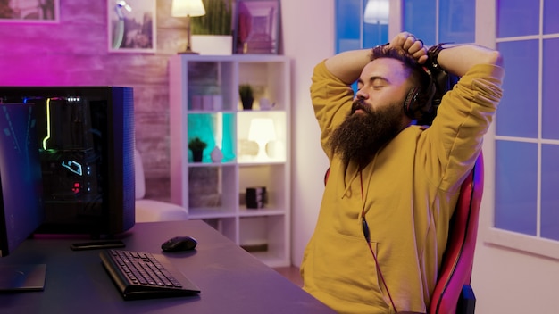 Счастливый бородатый мужчина после победы в онлайн-играх. Человек в наушниках во время игры в видеоигры.