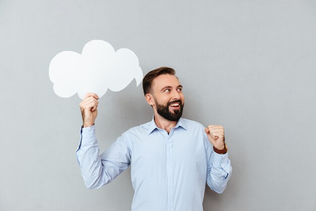 Happy bearded man in business clothes holding blank speech cloud