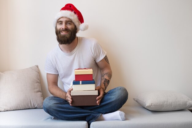 Happy bearded man wearing Santa hat and holding gift boxes