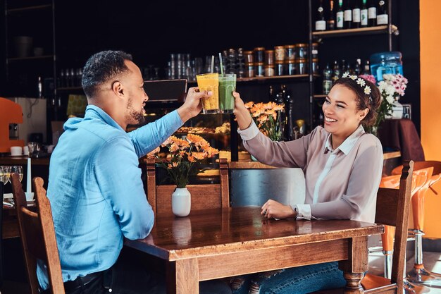 happy beautiful african-american couple in love having a great time together in a restaurant at their dating, an attractive couple enjoying each other, holds glasses of a juice.