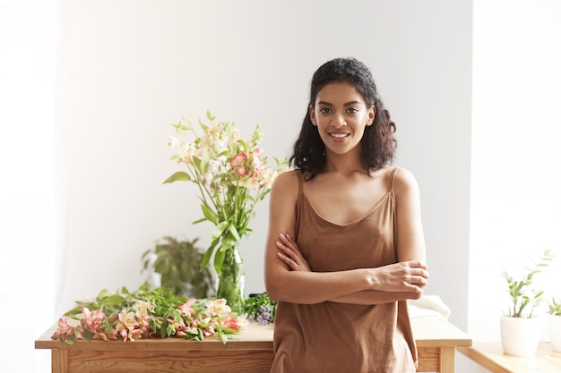 Happy beautiful african female florist smiling posing with closed eyes near workplace.