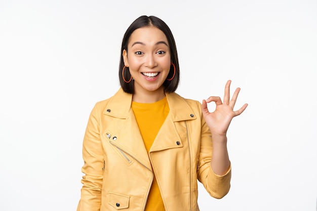 Happy beautiful asian girl shows okay ok recommending sign pleased by smth praising quality standing over white background