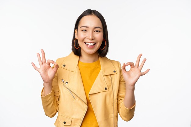 Happy beautiful asian girl shows okay ok recommending sign pleased by smth praising quality standing over white background