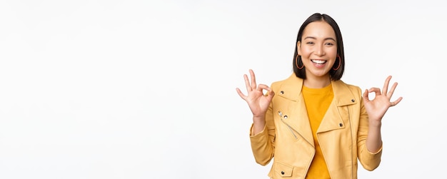 Happy beautiful asian girl shows okay ok recommending sign pleased by smth praising quality standing over white background