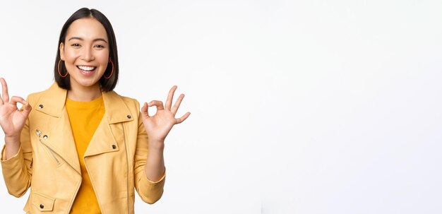 Happy beautiful asian girl shows okay ok recommending sign pleased by smth praising quality standing over white background