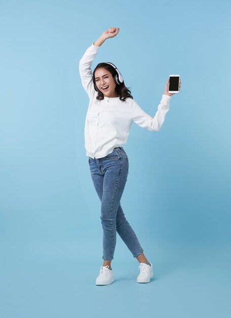 Happy beautiful Asian teen woman listening music on mobile phone wear headphones and dance