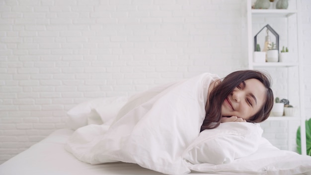 Happy beautiful Asian woman wake up, smiling and stretching her arms in her bed in the bedroom. 