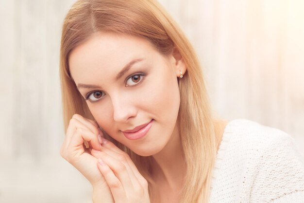 Happy beautiful blond lady in white dress looking at the camera. Pretty lady posing indoors.