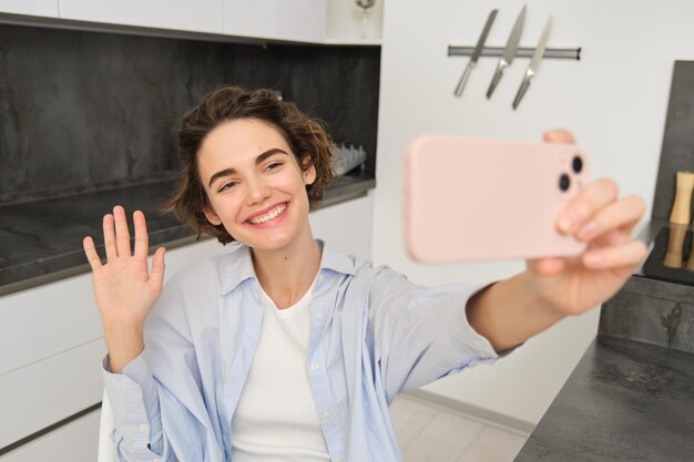 Happy beautiful brunette girl takes selfie at home poses for photo with smartphone