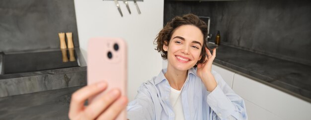 Free photo happy beautiful brunette girl takes selfie at home poses for photo with smartphone