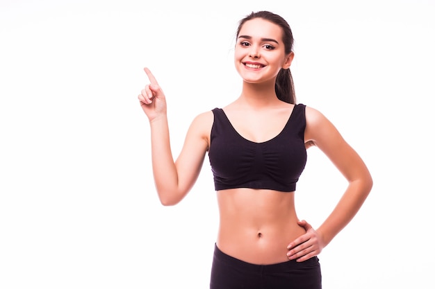 Happy beautiful fitness woman in sportswear pointing up at copyspace. Isolated on a white background