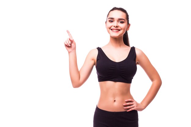 Happy beautiful fitness woman in sportswear pointing up at copyspace. Isolated on a white background