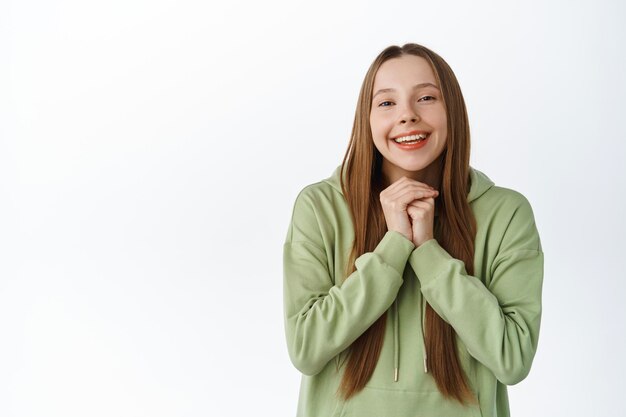 Happy beautiful gen-z girl with long hair, look with grateful and pleased face, say thank you, receive gift and gazing flattered, standing over white background.